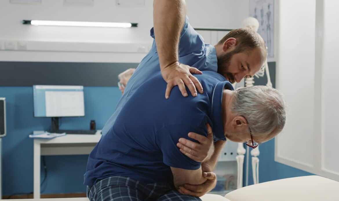 Osteopath helping senior man to crack back bones in cabinet
